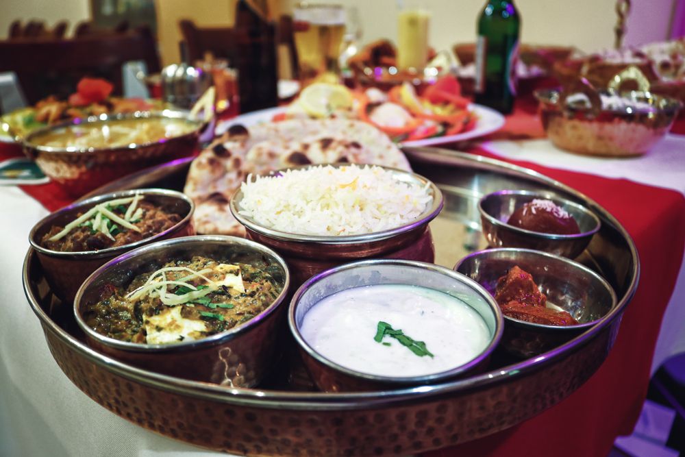 Indische Gerichte in Kupferschalen mit Reis und Naan auf einem Tablett