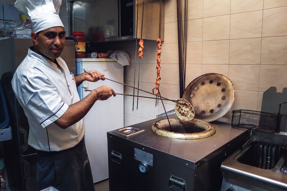 Koch am Tandoor-Ofen mit Fleischspießen und Naan